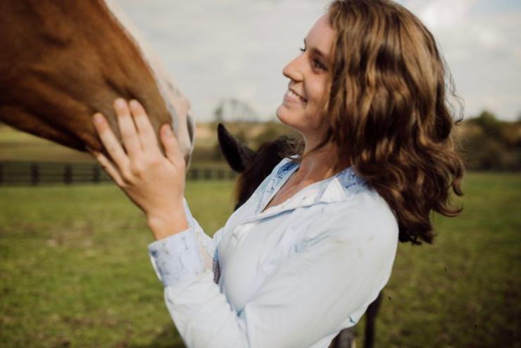 一个伯里的学生微笑着抚摸着田野里的一匹马