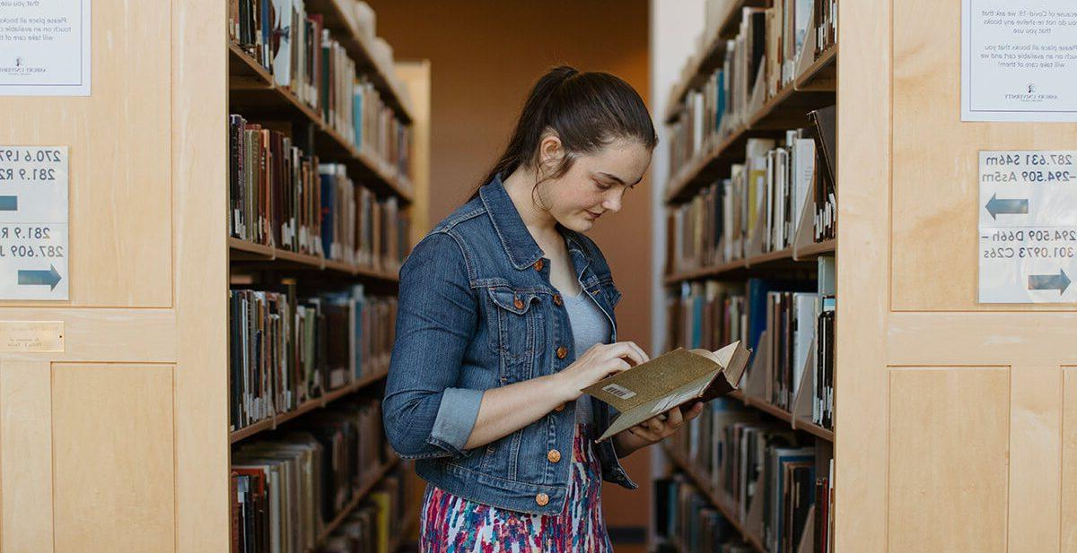 在博彩app推荐图书馆，一名女学生在一排排的书中间看书