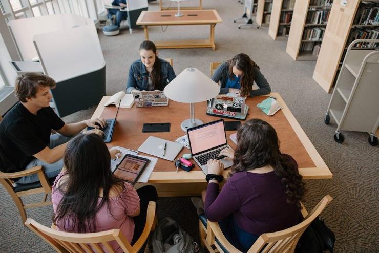 五个博彩app推荐的学生围坐在图书馆的桌子旁，拿出了他们的笔记本电脑