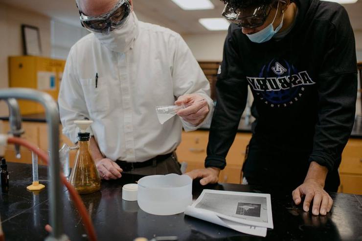 博彩app推荐的化学老师在教室实验室里指导穿着学校运动衫的学生